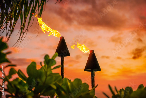 Hawaii luau party Maui fire tiki torches with open flames burning at sunset sky clouds at night. Hawaiian cultural travel vacation background. photo