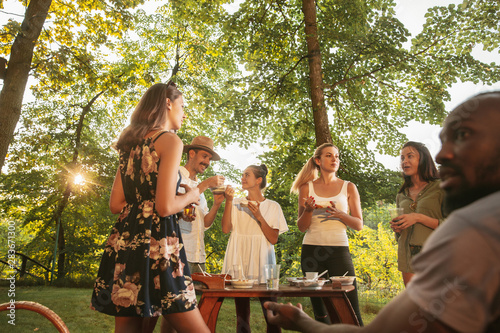 Canvas Print Group of happy friends eating and drinking beers at barbecue dinner on sunset time