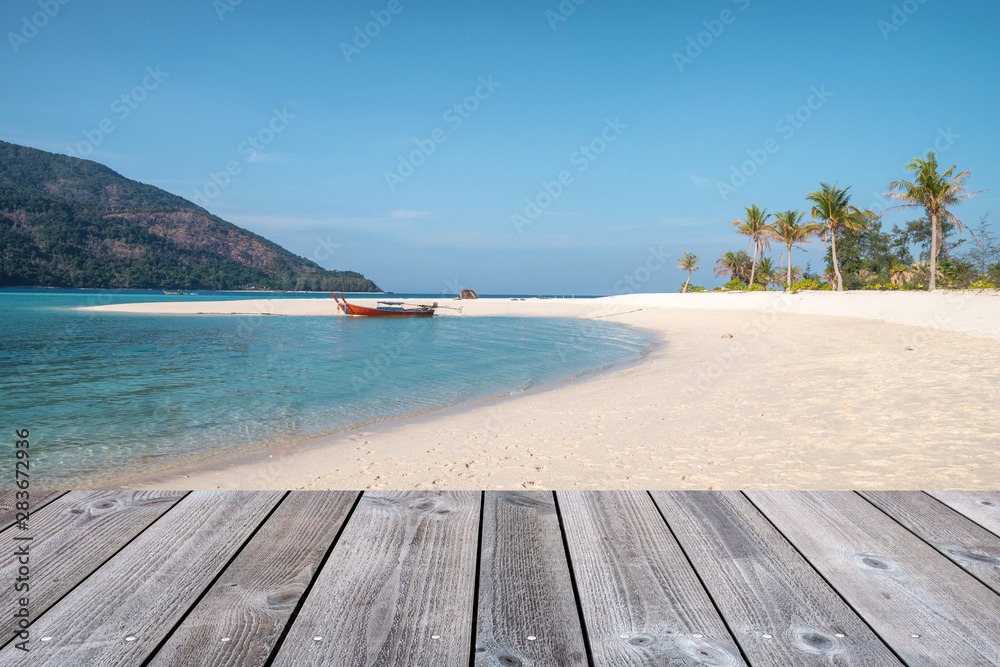 Fototapeta premium Wooden tabletop on white sand beach with wooden long-tail boat in tropical sea