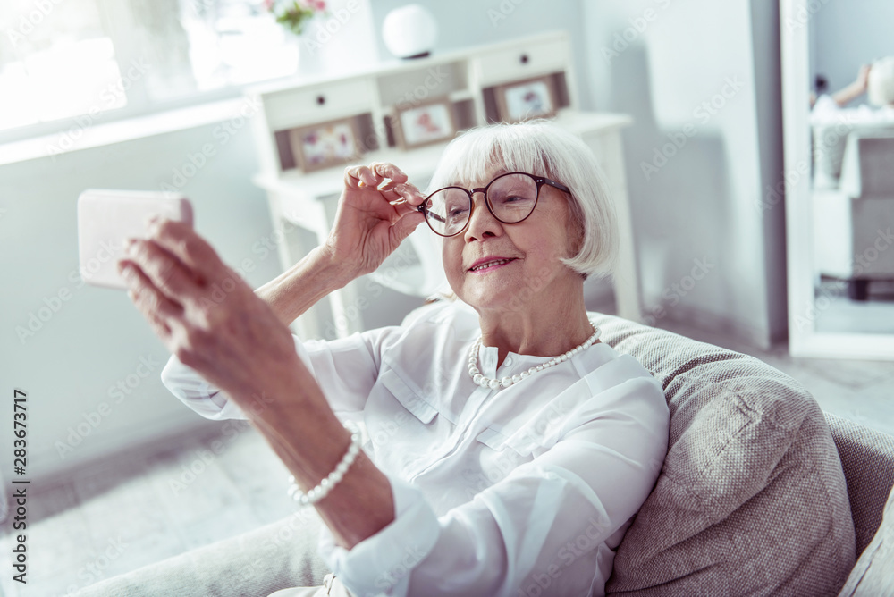 Fototapeta premium Stylish appealing retired woman holding her glasses while making selfie