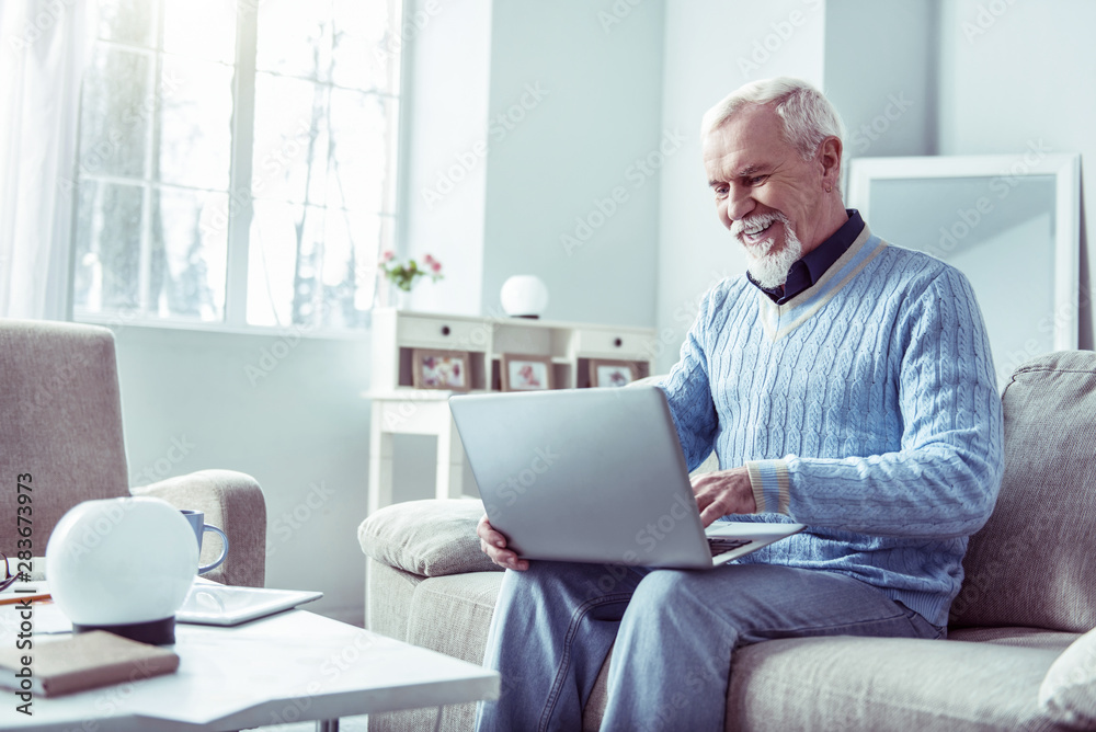 Smiling bearded retired man looking at laptop while having video chat Smiling bearded retired man looking at laptop while having video chat