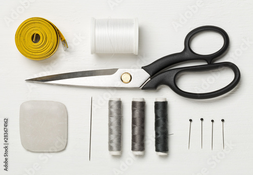 Flat lay top view sewing tools with measurement tape, chalk, thread, needles and scissors on white wood table photo
