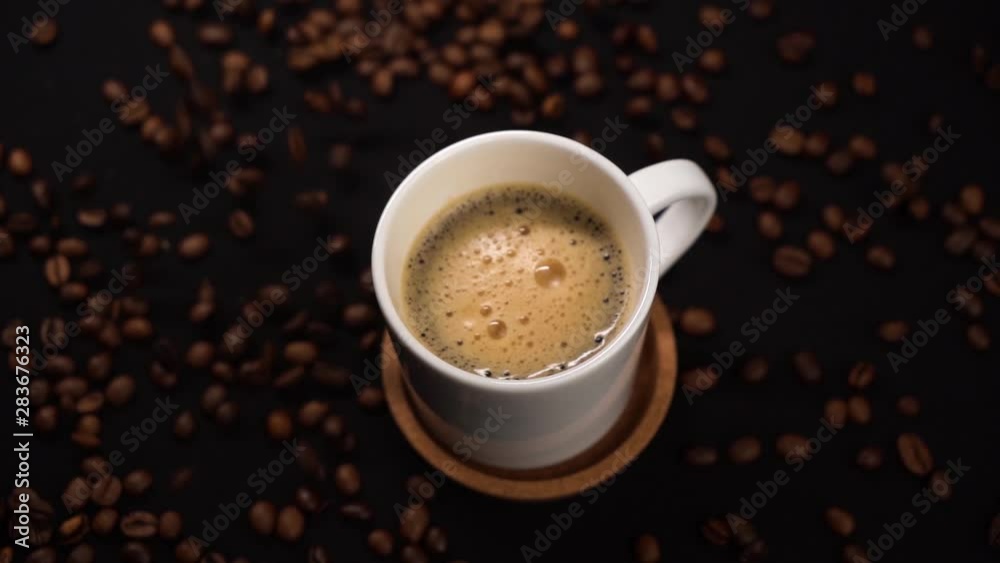 Top view of stirring coffee in white cup with spoon on black table with coffee beans on table. Top view of stirring coffee in white cup with spoon on black table with coffee beans on table.
