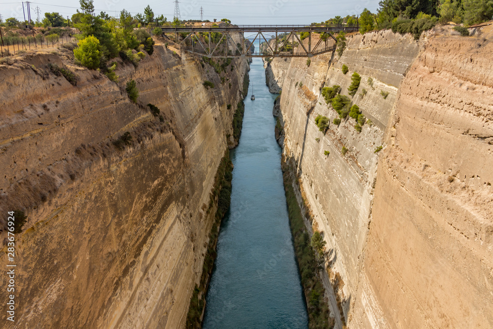 Small sailing boat passing through Corinth canal. The Corinth Canal connects the Gulf of Corinth with the Saronic Gulf in the Aegean Sea. It separates Peloponnese from the Greek mainland. Small sailing boat passing through Corinth canal. The Corinth Canal connects the Gulf of Corinth with the Saronic Gulf in the Aegean Sea. It separates Peloponnese from the Greek mainland.