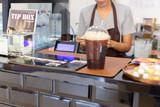 Selected focus cash register with woman barista working behind the counter bar.
