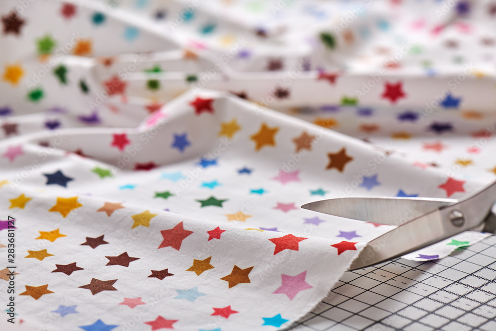Obraz premium Process cutting fabric with a pattern of colorful stars by scissors on craft mat
