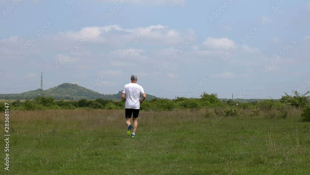 Middle aged sporty man running on the meadow in springtime Middle aged sporty man running on the meadow in springtime