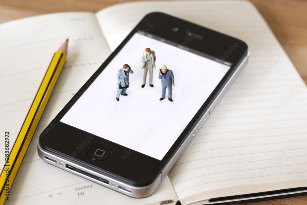 Miniature businessman standing on a cell phone with a pencil next to them having a business meeting and discussing strategys Miniature businessman standing on a cell phone with a pencil next to them having a business meeting and discussing strategys