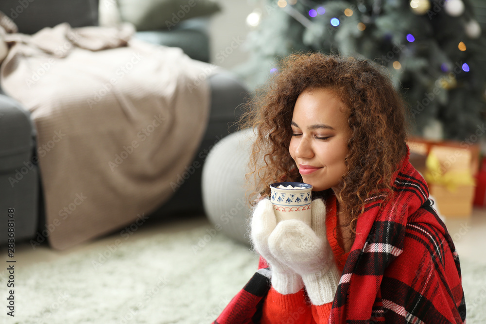 Obraz premium Young African-American woman drinking hot chocolate at home on Christmas eve