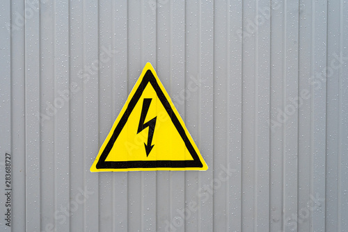 Triangular yellow sign of dangerous electrical voltage on the gray wall. Raindrop