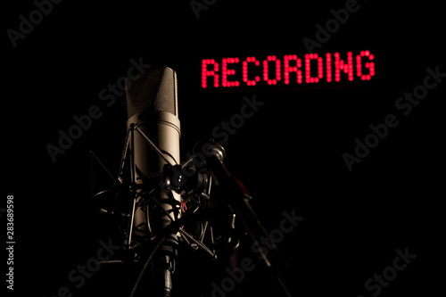 Mikrofon im dunklen Studio vor roter Recording Leuchtschrift im Hintergrund photo