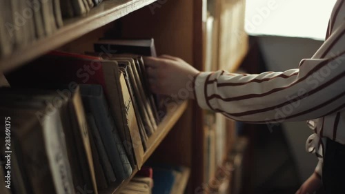 Close up of female hands looking for a book from a bookshelf in library