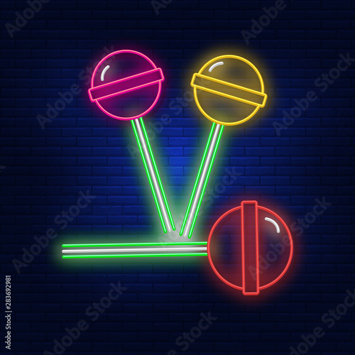 Neon illumination of sucking candy. Bright advertising candy on a stick. Modern logo vector, banner, Billboard, illustration of chocolates. Night advertising on the background of a brick wall.
