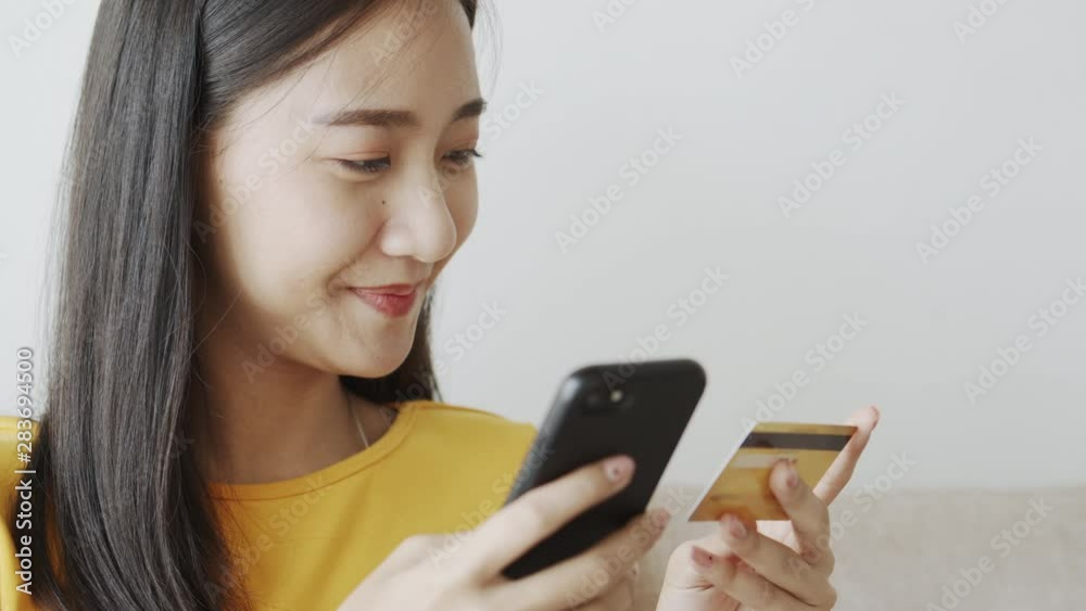 Close-up of Asian women are buying product online with a credit card. Asia girl are sitting using smartphone Via the internet transactions in the living room at home. Close-up of Asian women are buying product online with a credit card. Asia girl are sitting using smartphone Via the internet transactions in the living room at home.