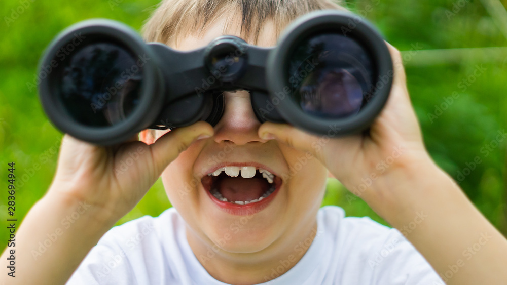 curious boy looks for wildlife through binoculars in the park.Exploring the world. Summer holidays. Outdoor activities. curious boy looks for wildlife through binoculars in the park.Exploring the world. Summer holidays. Outdoor activities.