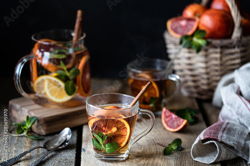 Homemade tea in a transparent glass with red orange and lemon, cinnamon and mint on a wooden background. Oranges Wicker Basket