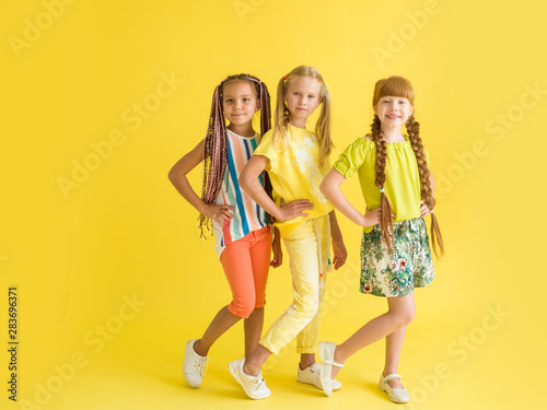 Three beautiful fashionable girls posing on a yellow background in full growth with a place for text. Children's summer fashion