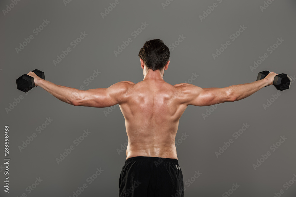 Handsome young strong sportsman posing isolated over grey wall background make exercises with dumbbells for arms. Handsome young strong sportsman posing isolated over grey wall background make exercises with dumbbells for arms.