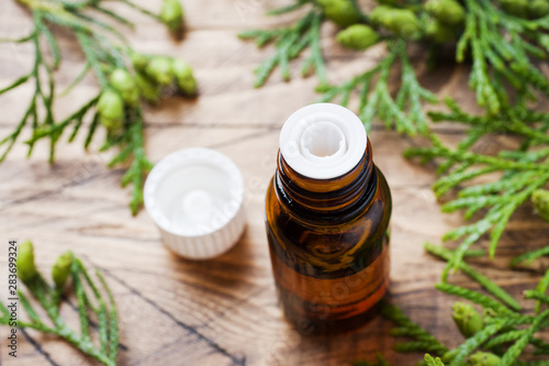 Thuja aroma essential oil in a glass jar on wooden background. Copy space. Selective focus.