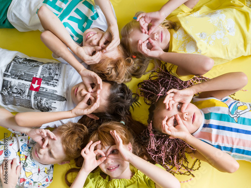 A group of children lying on their backs gaily look at the camera with their hands to their eyes in the form of glasses. Happy joyful children