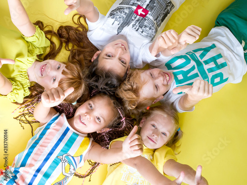 Group of beautiful cheerful children lie on their back looking at the camera holding their thumb up