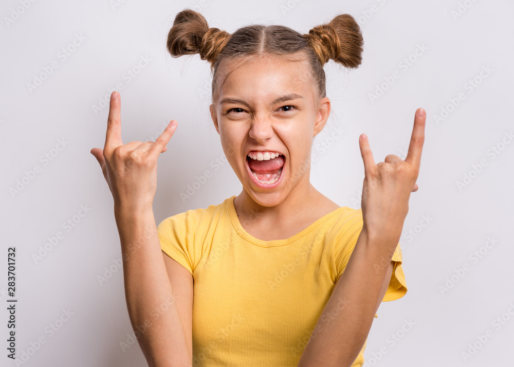 Portrait of funny teen girl making Rock Gesture, on gray background.  Beautiful caucasian young teenager showing horns up gesture. Happy cute  child screaming and doing heavy metal rock sign. foto de Stock