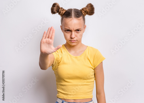 Portrait of teen girl doing stop sing with palm of hand, on gray background. Beautiful caucasian teenager making stop gesture with negative and serious facial expression. Angry child looking at camera