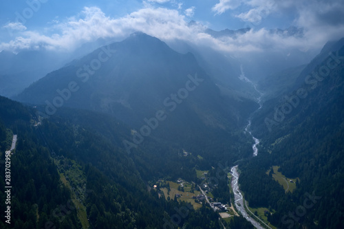 View of the mountain river. The river flows down the slope against the backdrop of alpine mountains in the snow. The popular ski resort town of Ponte di Legno. Photo taken on a drone.