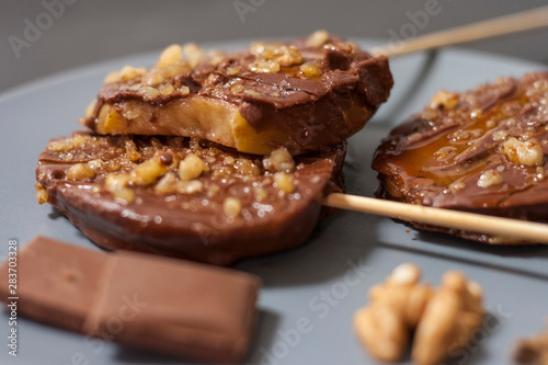 Slices of apples in chocolate  caramel glaze and walnuts on skewers on a dark background