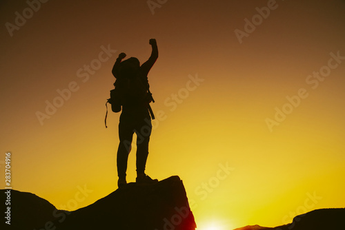 Man standing on edge of mountain feeling victorious with arms up in the air. Victory. Success, life goals