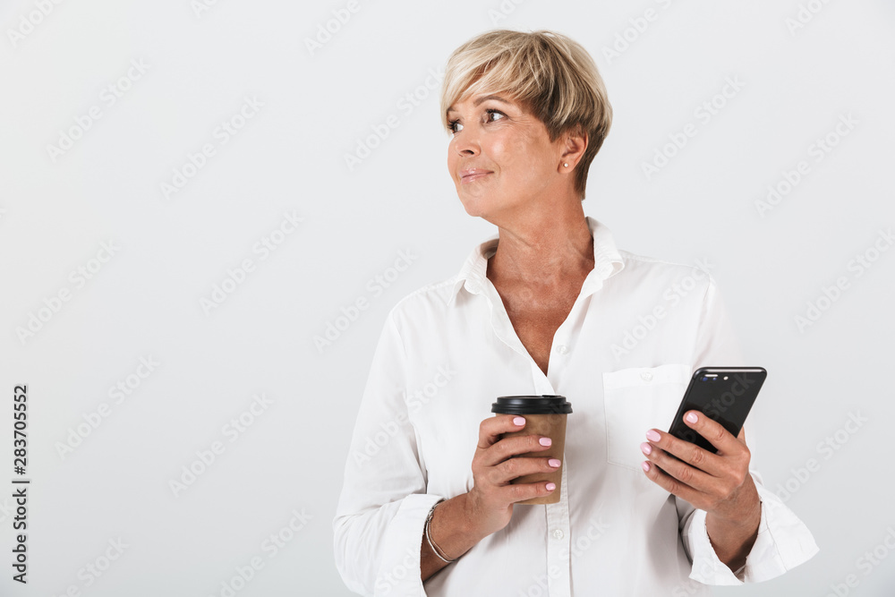 Portrait of charming adult woman with short blond hair holding cellphone and takeaway coffee cup Portrait of charming adult woman with short blond hair holding cellphone and takeaway coffee cup