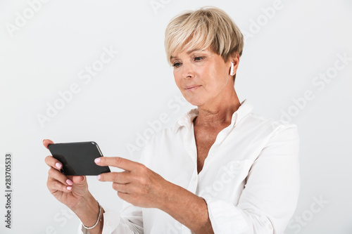 Image of elegant adult woman with short blond hair wearing earpods and holding cellphone