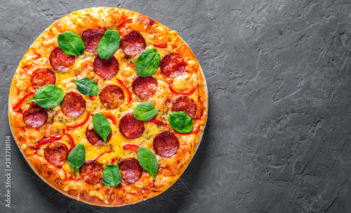 Pepperoni Pizza with Mozzarella cheese, salami, pepper, Spices and Fresh spinach. Italian pizza on Dark grey black slate background