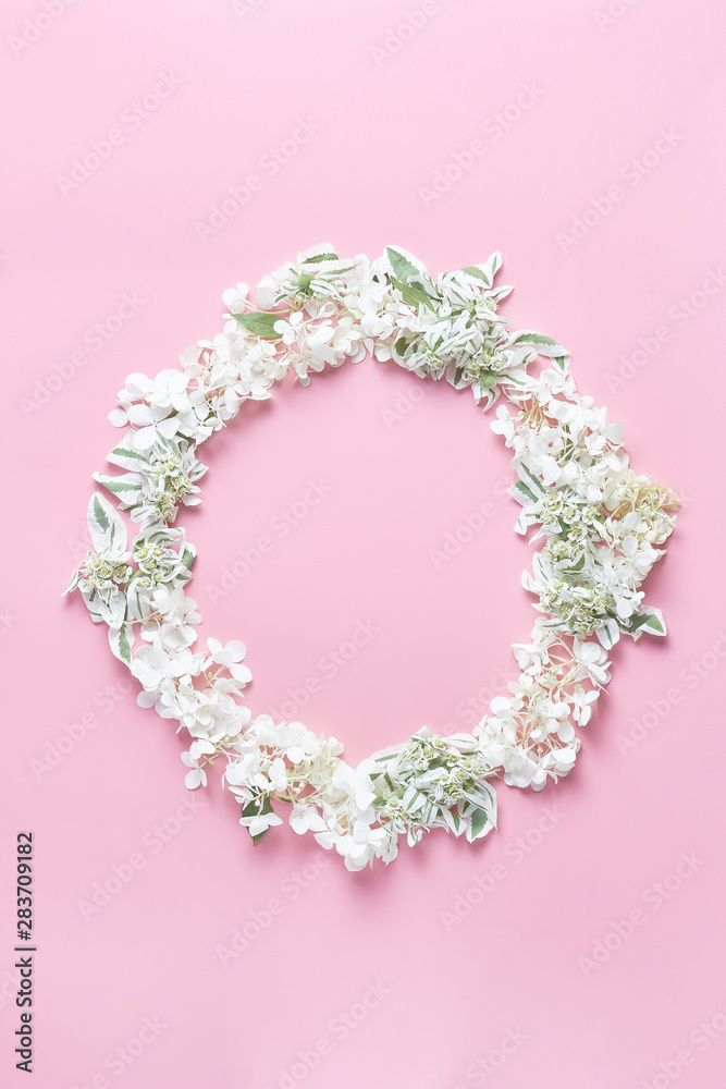 round frame wreath pattern on pink background. ornament with white fresh hydrangea flowers, petals, and green leaves. flat lay, vertical frame, copy space