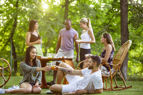 Canvas Print Group of happy friends eating and drinking beers at barbecue dinner on sunset time