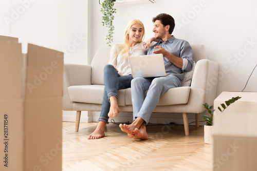 Couple Buying Furniture Online Sitting On Sofa In New Apartment