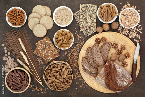 High fibre health food with whole wheat walnut and rye bread, whole grain pasta, oatmeal and seeded crackers, barley oats, bran flakes and wheat sheath on lokta paper background.