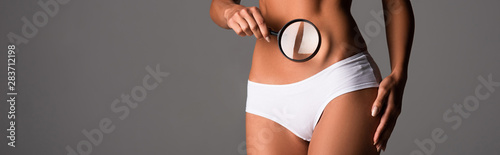 panoramic shot of sexy girl in white panties holding magnifying glass isolated on grey