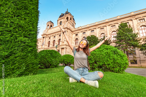 Photography Happy young woman sitting on a green lawn near historical architecture building in Vienna city, Austria