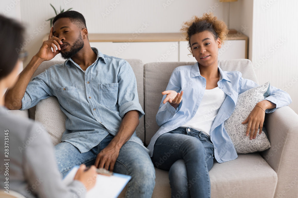 Indifferent Black Spouses Sitting On Sofa At Couples Therapist's Office Indifferent Black Spouses Sitting On Sofa At Couples Therapist's Office