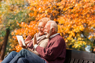 Happy senior couple talking with their grandkids via tablet in a