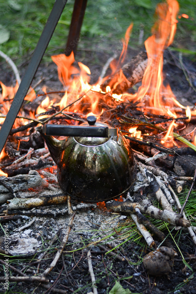 old shiny metal kettle basks on a fire, travel vacation weekend on a summer day old shiny metal kettle basks on a fire, travel vacation weekend on a summer day