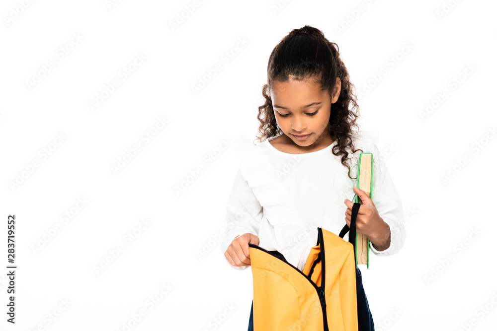 cute african american schoolgirl looking into backpack while holding book isolated on white cute african american schoolgirl looking into backpack while holding book isolated on white
