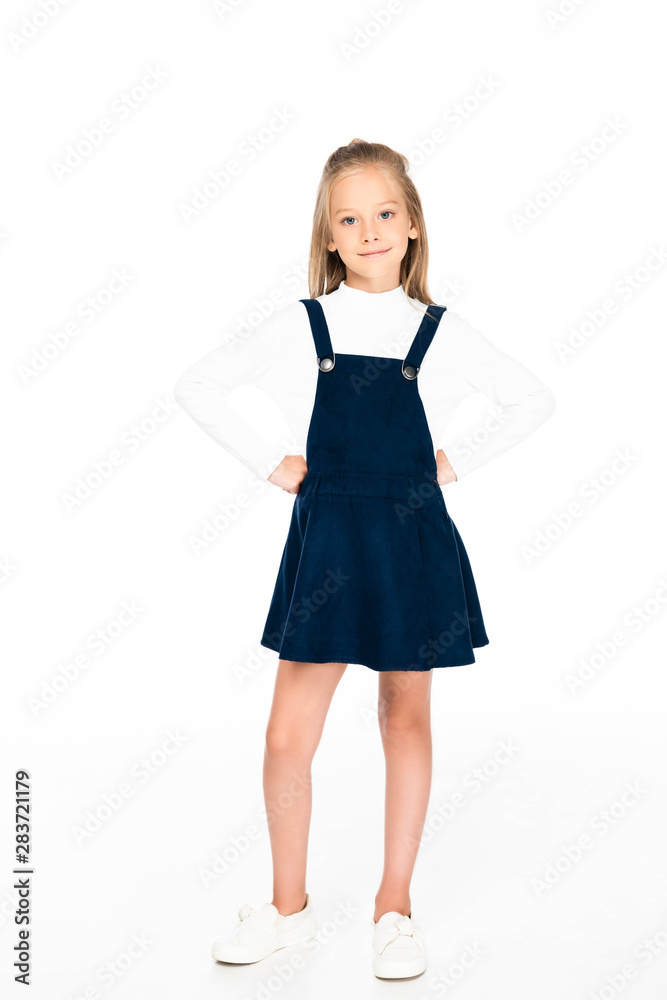 full length view of cute schoolgirl holding hands on hips while posing at camera on white background full length view of cute schoolgirl holding hands on hips while posing at camera on white background