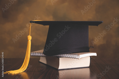 A mortarboard and graduation scroll, tied with red ribbon, on a stack of old battered book with empty space to the left. Slightly undersaturated with vignette for vintage effect. photo