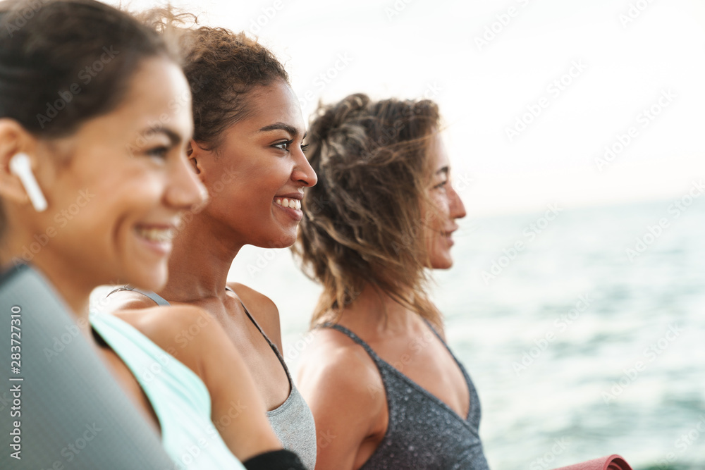 Three cheerful young sport girls standing at the beach