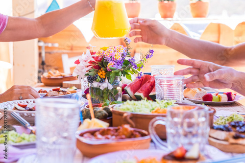 Sharing food and drink with the family. Caucasian peoples enjoying brunch or meal together. Fruits and vegetables on the wooden table. Sunlight outdoor on the terrace