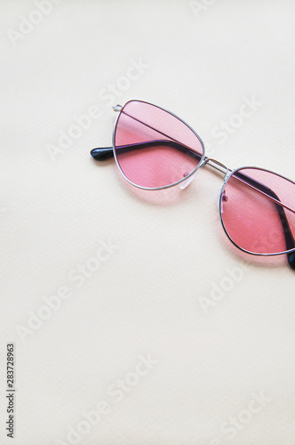 Pink sunglasses on beige paper background. Warm colors and shades