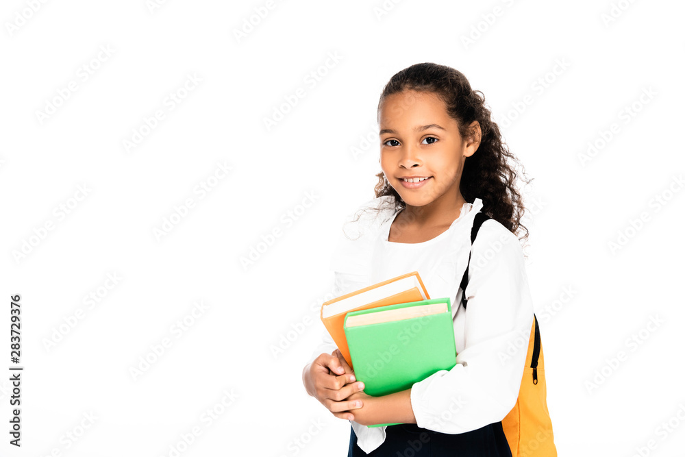cute, cheerful african american schoolgirl holding book and looking at camera isolated on white cute, cheerful african american schoolgirl holding book and looking at camera isolated on white