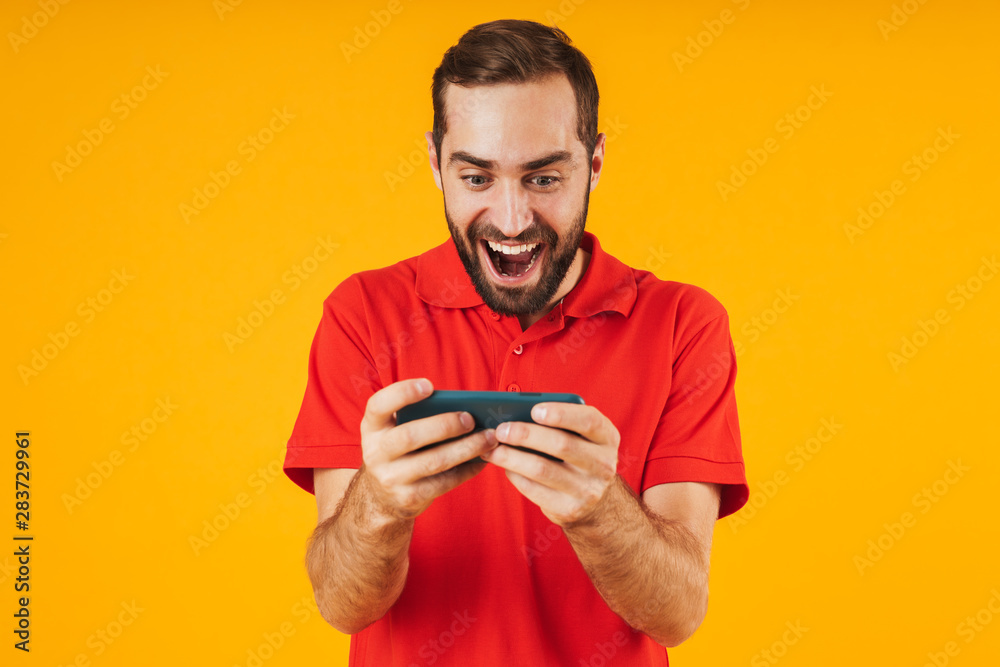 Portrait of handsome man in red t-shirt smiling and holding smartphone while playing video games Portrait of handsome man in red t-shirt smiling and holding smartphone while playing video games